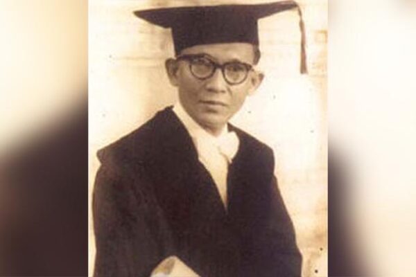 Wiyoto Wiyono mengenakan toga wisuda dan kacamata dalam foto hitam-putih