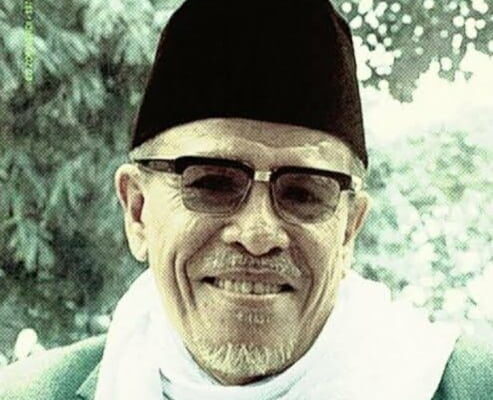 Buya Hamka tersenyum mengenakan peci hitam dan kacamata