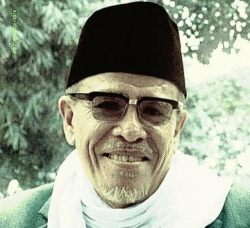 Buya Hamka tersenyum mengenakan peci hitam dan kacamata