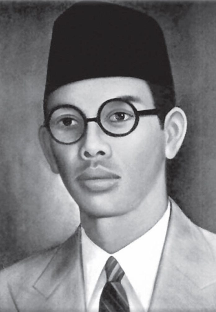 Potret hitam putih WR Soepratman memakai peci dan kacamata bundar.