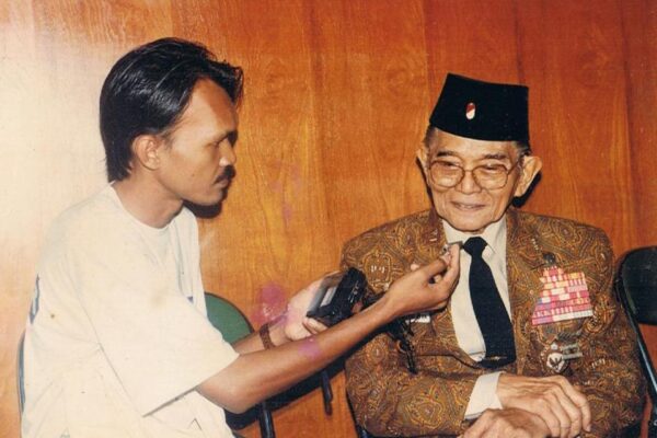 Andi Mattalatta diwawancarai wartawan, mengenakan jas batik dan peci.