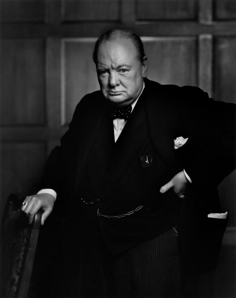 Winston Churchill berdiri dengan ekspresi tegas mengenakan setelan jas gelap